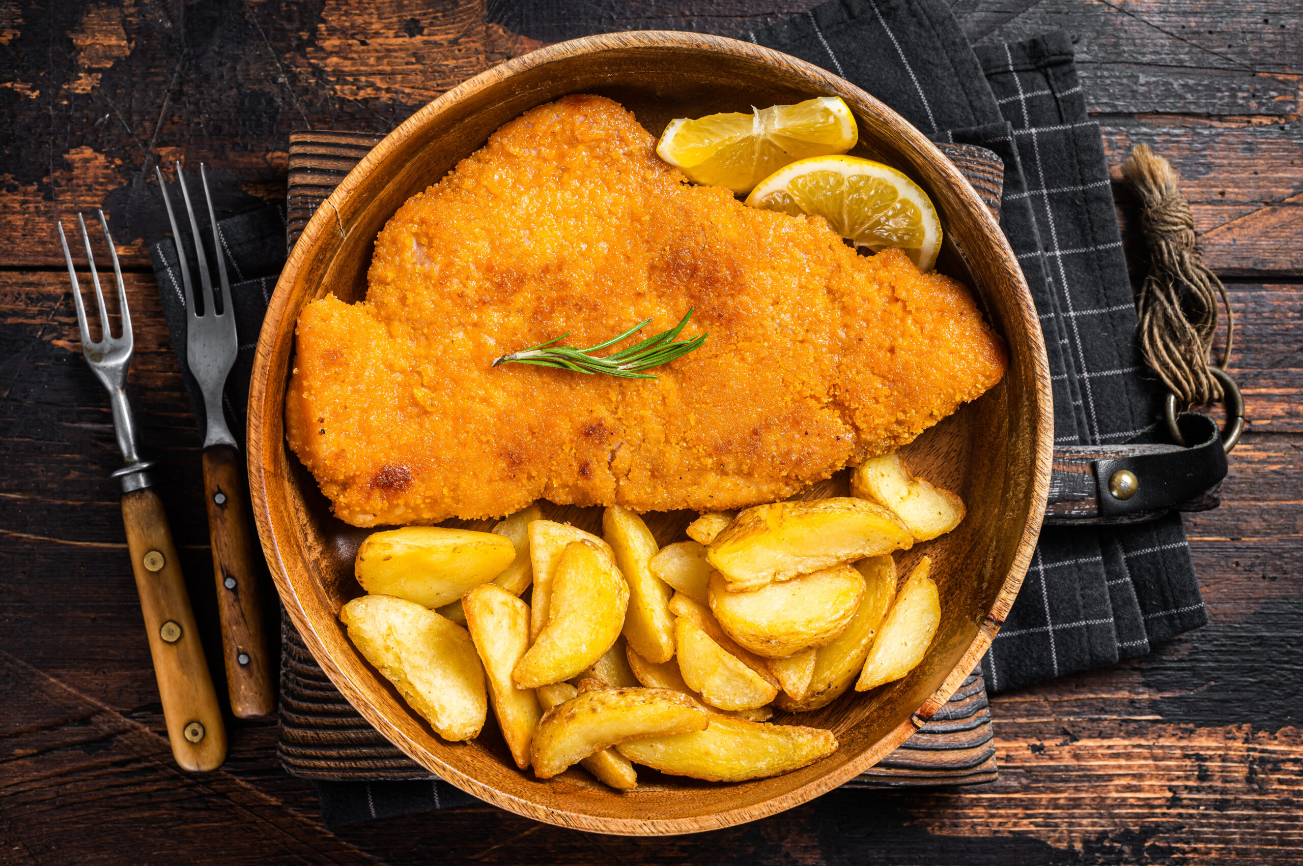 Austrian fried weiner schnitzel with potato wedges in a wooden plate. Wooden background. Top view.