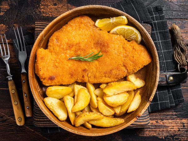 Austrian fried weiner schnitzel with potato wedges in a wooden plate. Wooden background. Top view.